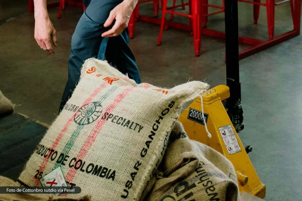 ¿Pueden los nuevos aranceles de Trump convertirse en una oportunidad para Colombia? 2 Sacos de café con sello de Colombia sobre montacargas en centro logístico, una posible ventaja según AmCham ante los aranceles de Trump.