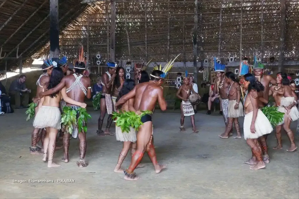Grupo de indígenas amazónicos bailando con trajes tradicionales en una maloca.