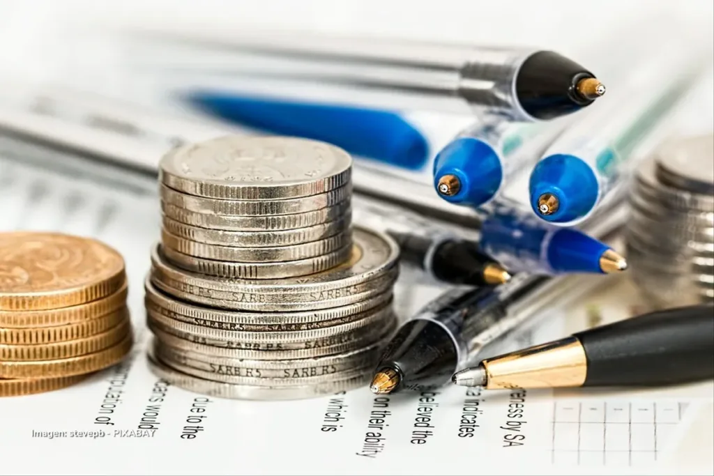 Desigualdad económica, rezago productivo y transición energética: ¿puede Colombia ser competitiva? 3 Monedas apiladas y bolígrafos sobre documentos financieros, ilustración del desarrollo productivo en Colombia.