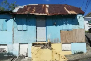 Fachada de casa deteriorada con paredes azules y techo oxidado, muestra visual de la desigualdad económica en Colombia.
