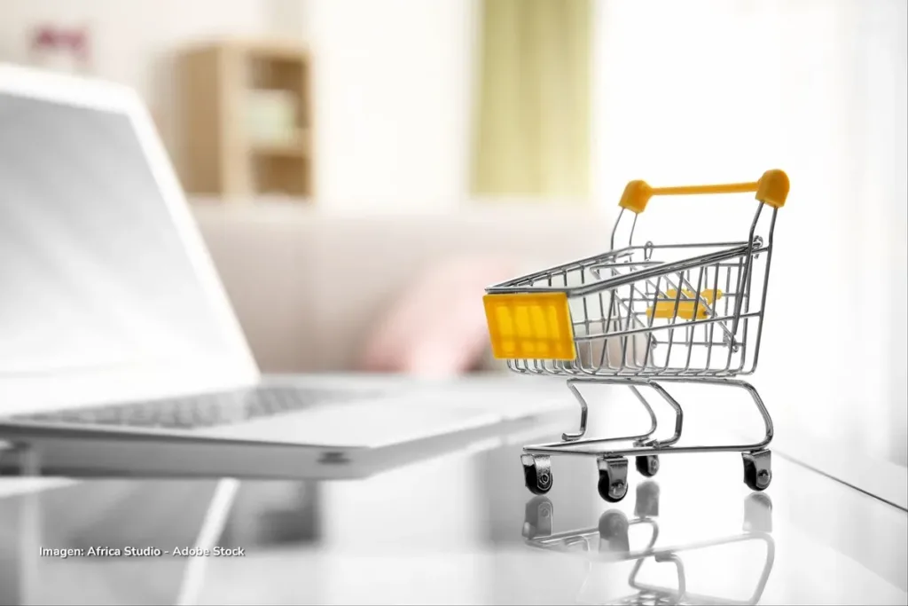 El cuidado frena los micronegocios de las mujeres en Colombia: venden 40% menos 3 Carrito de compras en miniatura sobre mesa junto a portátil, símbolo de los emprendimientos desde casa en Colombia.