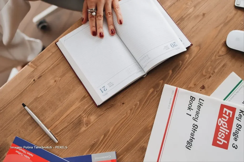 Cuaderno abierto y libros de English sobre escritorio; clases de inglés gratis.