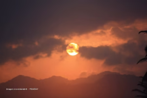 Sol intenso entre nubes oscuras sobre montañas durante la ola de calor 2025.
