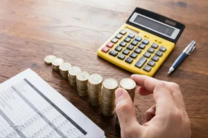 Mano organiza monedas junto a calculadora y tabla de cifras, vinculada al Observatorio Fiscal.