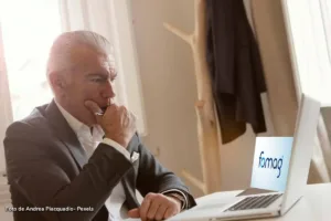 Hombre mayor observa con preocupación el logo del Fomag en la pantalla de su computador, relacionado con la prima de mitad de año.