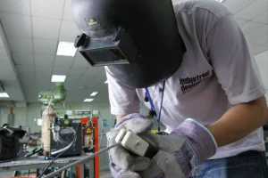 Trabajador con careta protectora realiza labores de soldadura en taller industrial, representando la reindustrialización en Colombia.