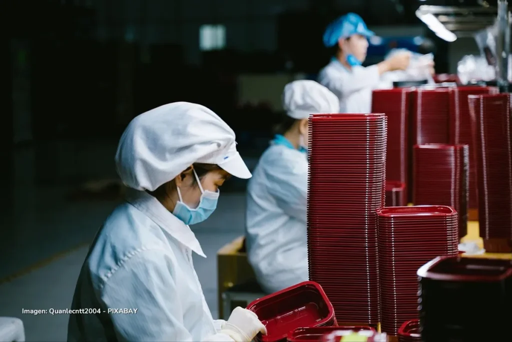 Producción industrial en fábrica china con operarias ensamblando envases plásticos rojos.