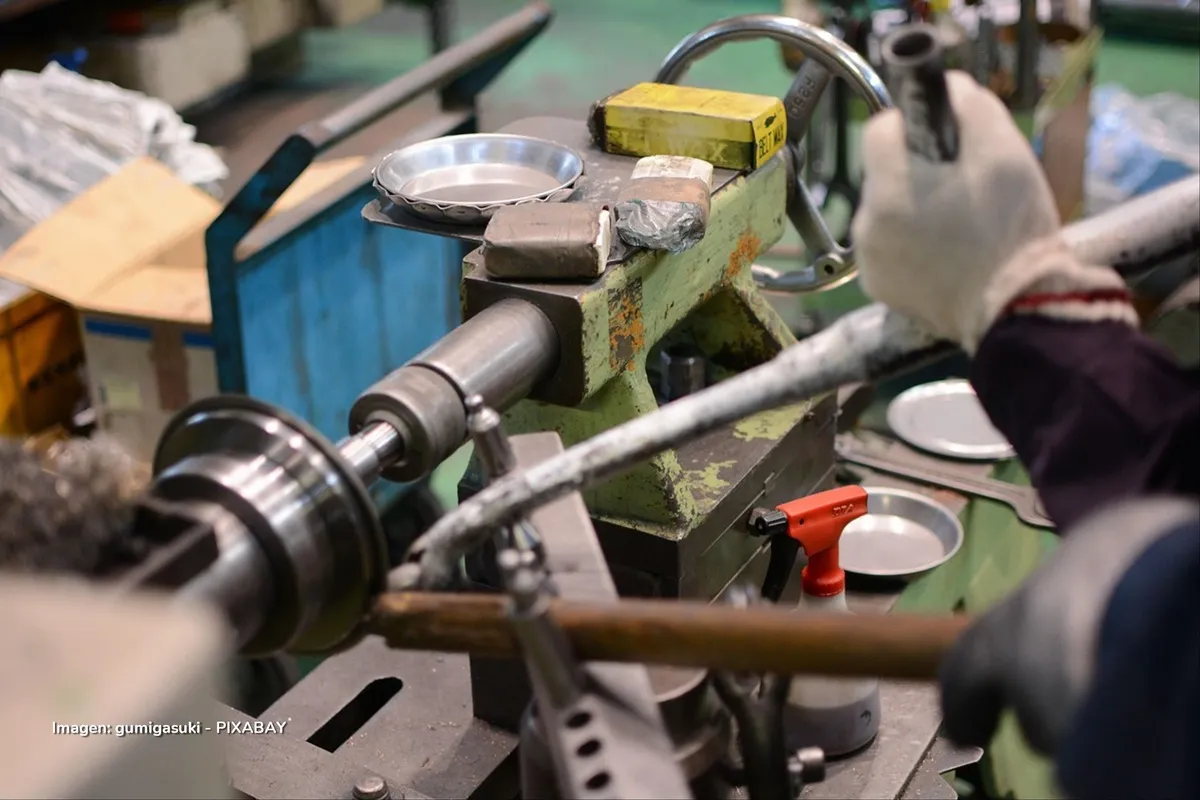 Operario en fábrica utilizando maquinaria industrial para producción de piezas metálicas, parte del sector manufacturero en Colombia.