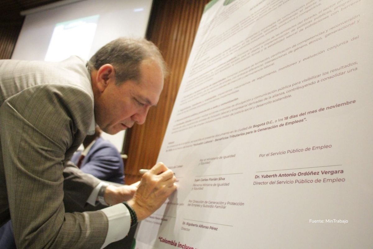 prima de navidad 2025. Funcionario firma un documento oficial de gran formato durante un evento institucional en un auditorio.