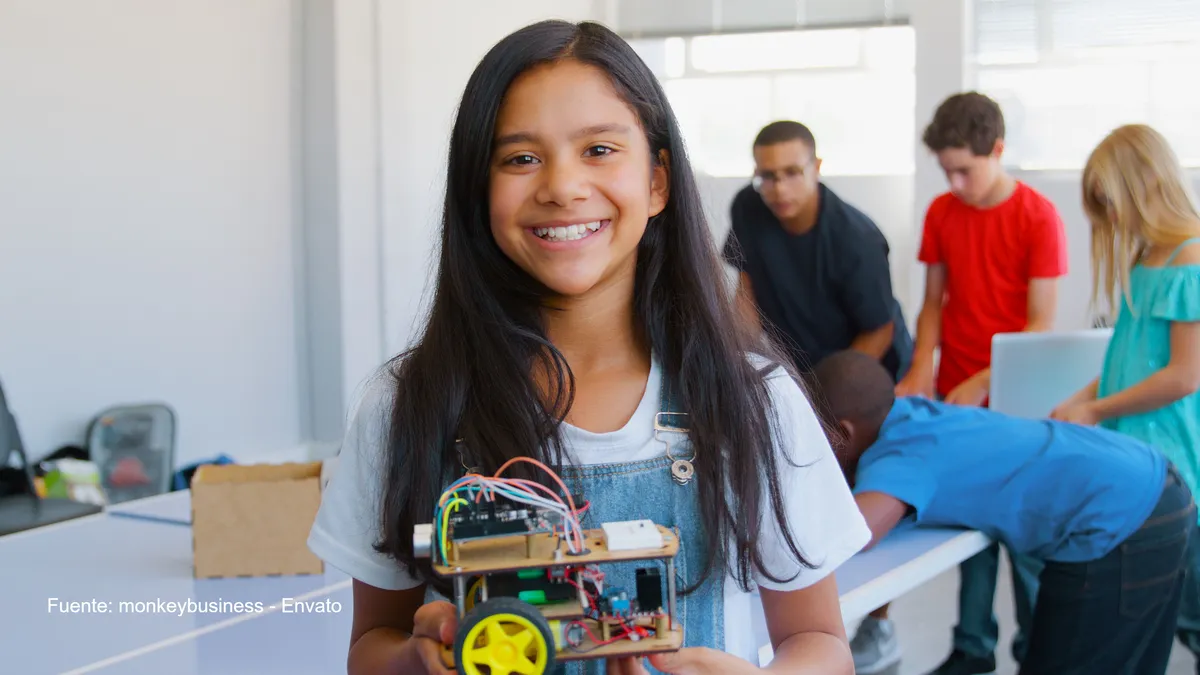 Inteligencia artificial: así está el ranking de adopción en América Latina según el ILIA 2025 2 Estudiante sonriente sosteniendo un robot hecho con componentes electrónicos y sensores, mientras otros niños trabajan en proyectos de inteligencia artificial.
