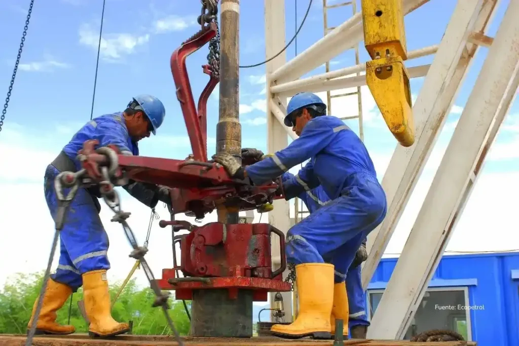 Trabajadores petroleros con casco y overol azul operan maquinaria pesada en una plataforma de perforación. Crisis Ecopetrol 2025