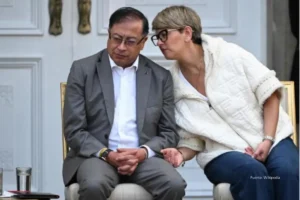 Dos personas sentadas conversando durante un acto público, una de ellas inclinada hacia la otra mientras hablan.