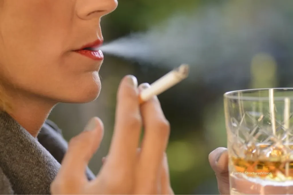 Persona sosteniendo un cigarrillo exhala humo mientras tiene en la otra mano un vaso de licor. ley de financiamiento 2025