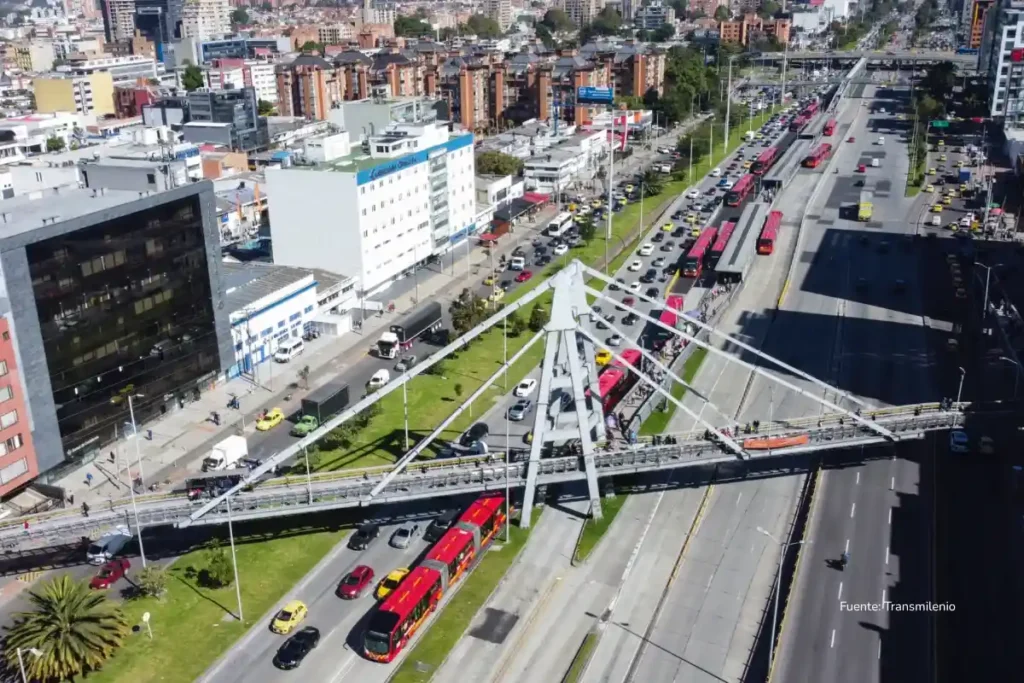 Vista aérea de una avenida en Bogotá con buses de TransMilenio, tráfico y un puente peatonal sobre la calzada. Aumento salario mínimo 2026