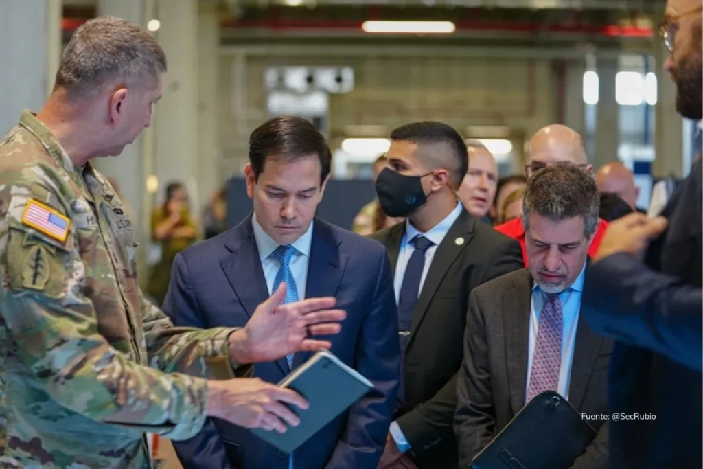 Militar con uniforme de camuflado explica información en una tableta a un grupo de funcionarios vestidos de traje durante una visita oficial.