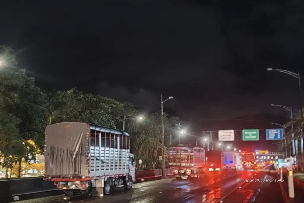 Caravana de camiones circulando de noche por la vía al Llano bajo lluvia y señalización luminosa.