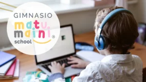 Un niño con audífonos azules utiliza un computador portátil en un escritorio, acompañado del logo de un colegio.