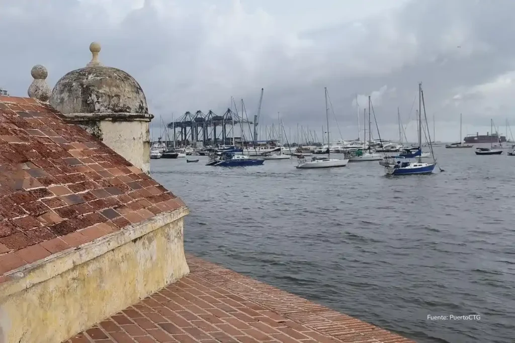 Lo que casi nadie cuenta del Puerto de Cartagena, el segundo puerto más eficiente del planeta 2 Vista de la bahía con embarcaciones menores y, al fondo, grúas portuarias y terminal marítima, junto a una estructura histórica de piedra en primer plano.
