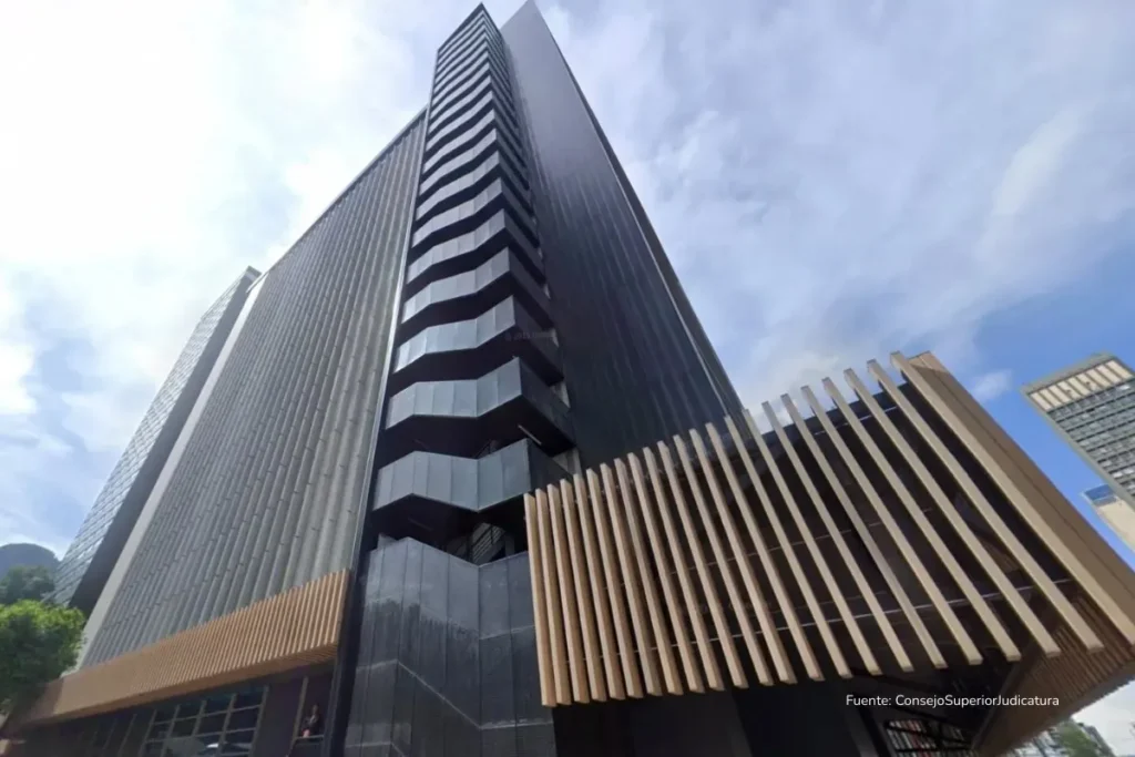 Caso UNGRD: por qué Ricardo Bonilla y Luis Fernando Velasco terminaron tras las rejas 2 Vista en contrapicado de un edificio institucional moderno del sector judicial, con fachada de vidrio y concreto, bajo un cielo parcialmente nublado.