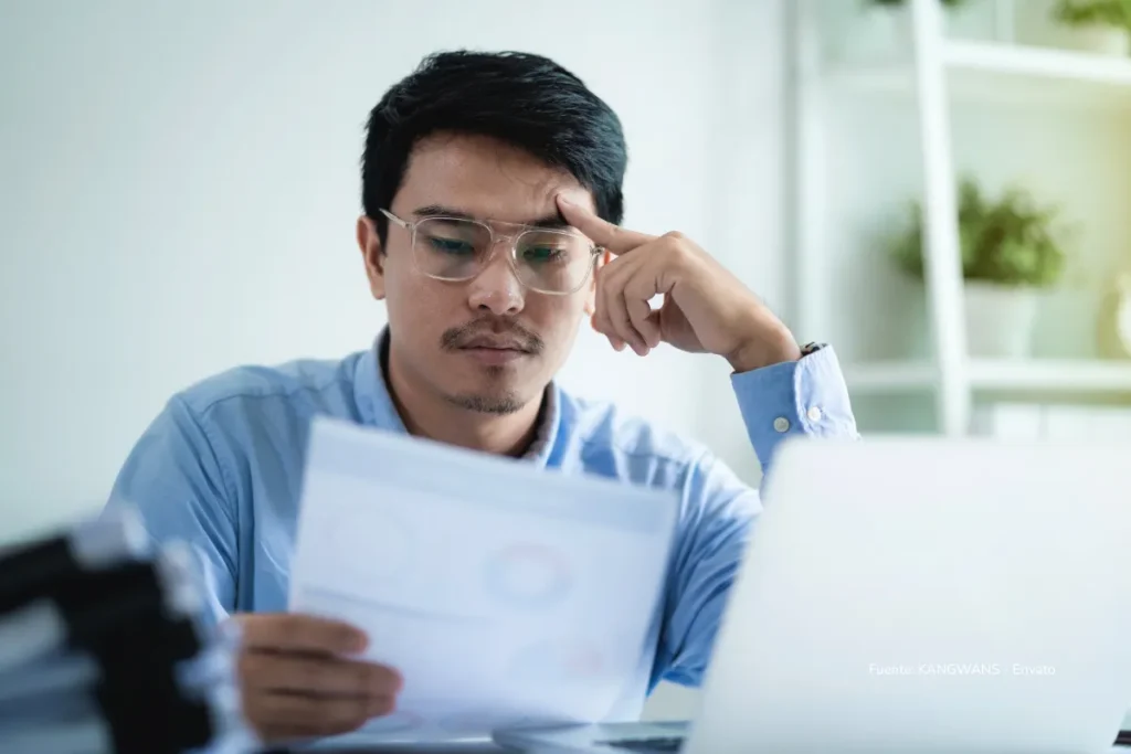 Intereses de cesantías: lo que debe hacer antes del 31 de diciembre para no perder dinero en 2026 2 Hombre revisando documentos con expresión de preocupación frente a su computador en un entorno de oficina.
