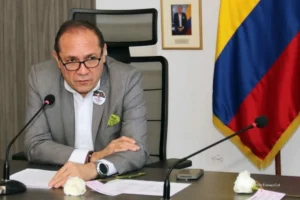 Cómo conseguir trabajo en 2026. Funcionario del Gobierno participa en una rueda de prensa o reunión oficial, sentado frente a un micrófono con la bandera de Colombia al fondo.