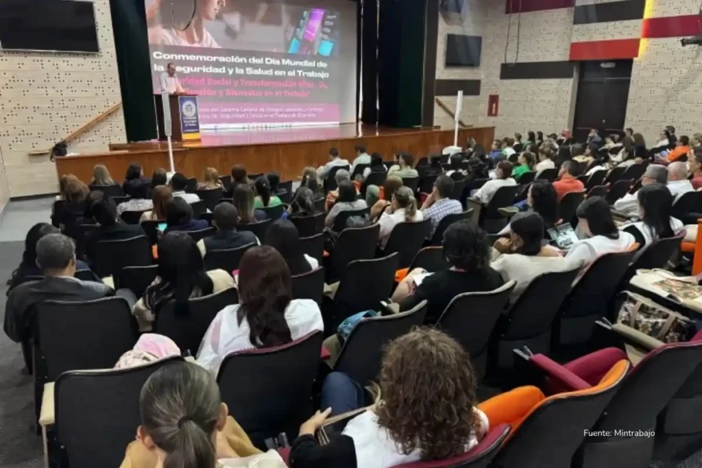 Cómo conseguir trabajo en 2026: la IA no te va a quitar tu empleo, alguien que sepa usarla sí 2 Auditorio lleno durante una conmemoración institucional sobre seguridad y salud en el trabajo, con una presentación proyectada al frente.