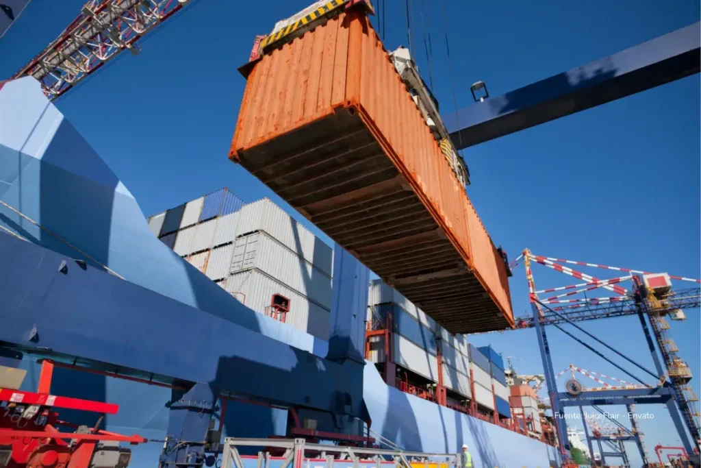 La verdad sobre por qué no verás huevo colombiano en Estados Unidos ni en un solo supermercado 3 Un contenedor naranja suspendido por una grúa portuaria mientras es cargado en un buque de transporte de mercancías.