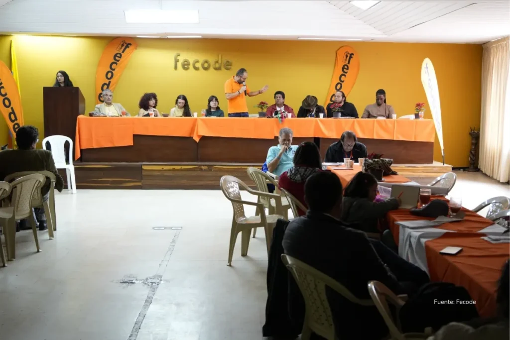 Mesada 14 docentes: el Senado dio un paso histórico y esto cambia para los maestros desde hoy 4 Autoridades y delegados de Fecode participan en una sesión de trabajo alrededor de una mesa en forma de U, con manteles naranjas y blancos, laptops y documentos frente a ellos.