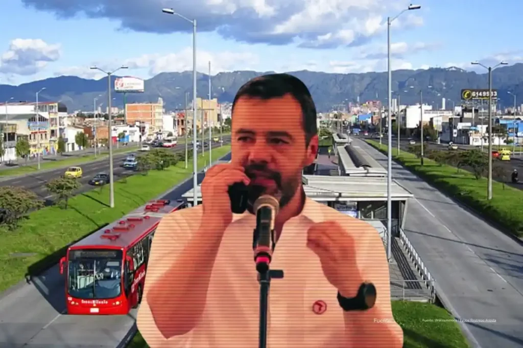 Funcionario habla frente a un micrófono con una vía urbana y buses de transporte público al fondo.