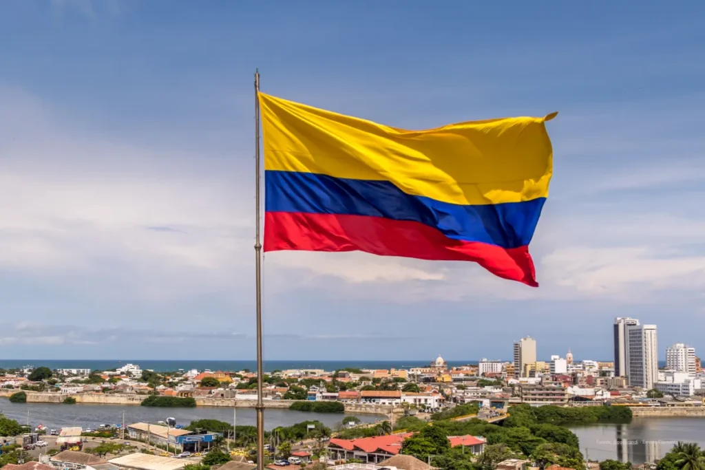 Aranceles de Colombia a Ecuador: el decreto que redefine el comercio bilateral 4 aranceles de Colombia a Ecuador. Bandera de Colombia ondeando sobre una ciudad costera con edificaciones y río al fondo