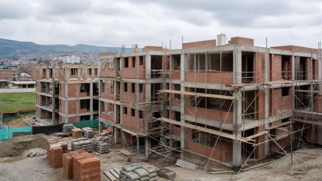 Edificio de vivienda en construcción con andamios, ladrillo a la vista y sacos de cemento