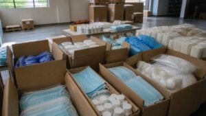 Fotografía editorial horizontal 16:9 de cajas abiertas con suministros médicos genéricos, paquetes sellados y material d