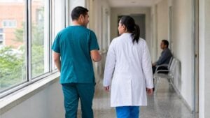Personal de salud camina por el pasillo de un centro de atención médica corriente.