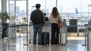 Dos viajeros de espaldas con maletas ante un mostrador de documentos en un aeropuerto