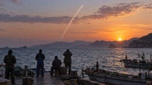 Pescadores observan desde un muelle una estela blanca sobre el mar al atardecer.