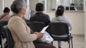 Una mujer mayor espera con una bolsa de medicamentos en la sala de un centro de salud.