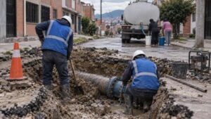 Operarios reparan una tubería mientras vecinos llenan baldes junto a un carrotanque en una calle de Bogotá