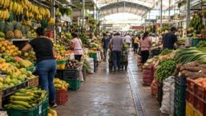 Vendedores y compradores recorren puestos de frutas y verduras en una plaza de mercado colombiana.
