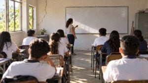 Docente y estudiantes en un salón rural con luz natural y una grieta en la pared lateral.