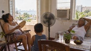Una familia se refresca con un ventilador y un aire acondicionado de ventana en una casa del Caribe durante una tarde calurosa.