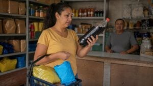 Compradora observa una gaseosa en una tienda de barrio con galletas y papas en los estantes