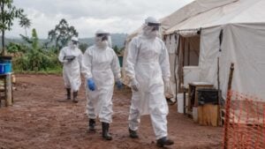 trabajadores de salud con trajes de protección blancos y careta caminan junto a una carpa de aislamiento en un centro de tratamiento rural en el este del Congo.