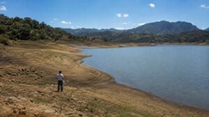 Persona observa un embalse colombiano genérico con nivel bajo visible bajo el sol
