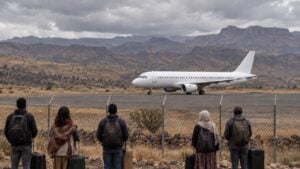 Viajeros esperan junto a la reja de un aeropuerto del norte de Etiopía con un avión detenido en la pista.