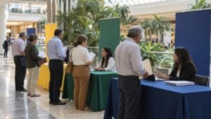 Personas adultas con hojas de vida conversan con asesoras en una feria de empleo dentro de un centro comercial.