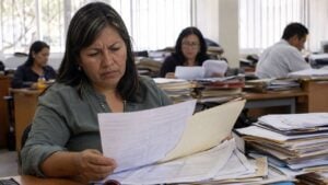 Docente revisa trámites médicos mientras personal administrativo organiza carpetas en una oficina