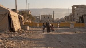 Familia camina con bultos junto a carpas y bloques amarillos en una calle de tierra de Gaza