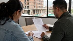 Pareja revisa documentos de vivienda en una sala de ventas frente a una obra
