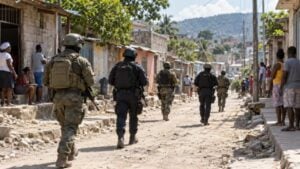 Soldados y policías de una fuerza multinacional patrullan una calle de tierra de un barrio de Puerto Príncipe mientras los vecinos observan.