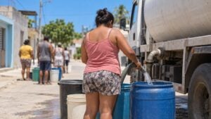 Mujer de espaldas llena canecas de agua de un carrotanque bajo el sol en un barrio de Santa Marta